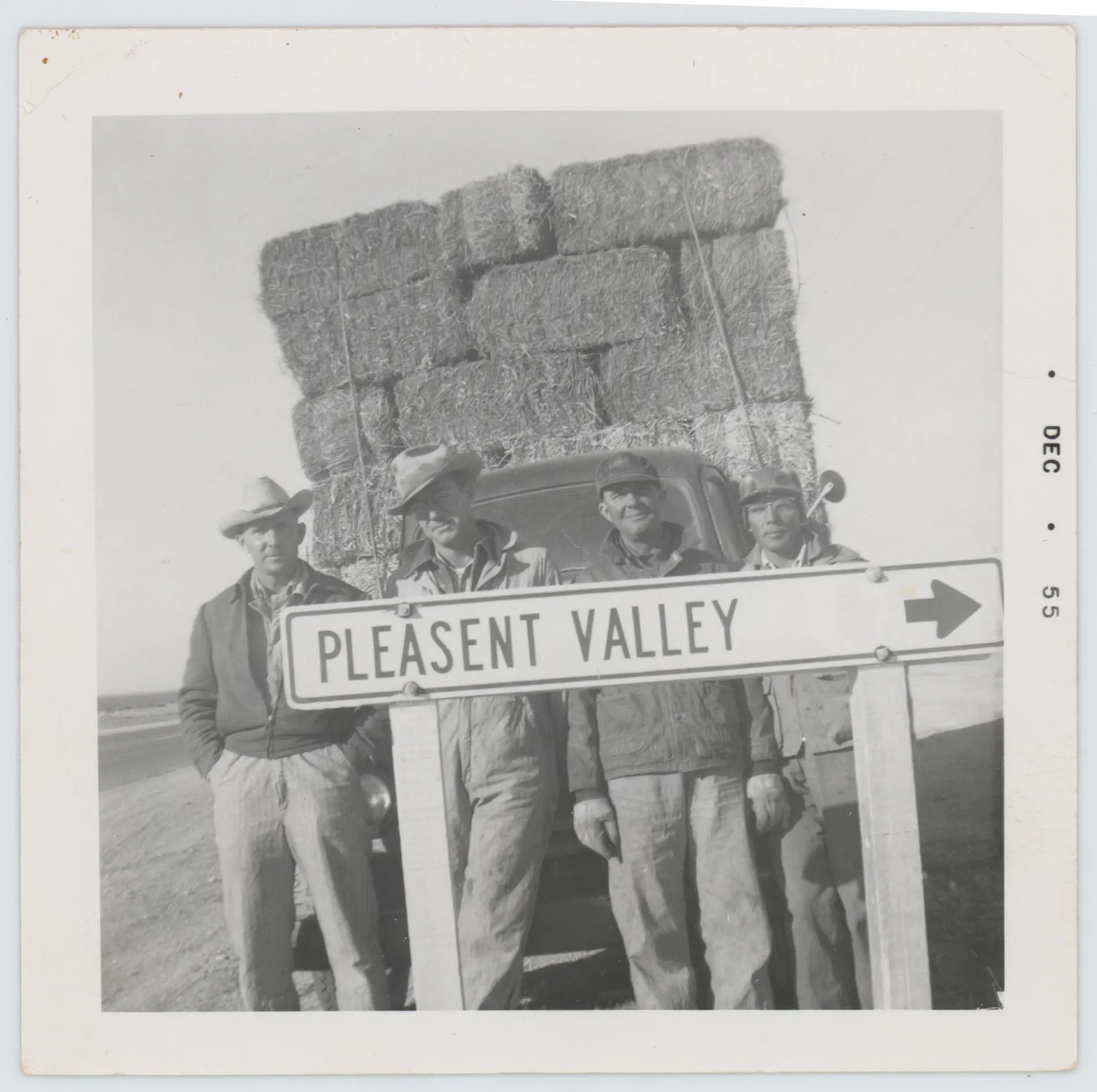 This photograph depicts Harold and Oscar Allison standing with two other men next to a sign that says "Pleasent Valley." A date of December 1955 is printed on the right side. The other two men are unidentified.