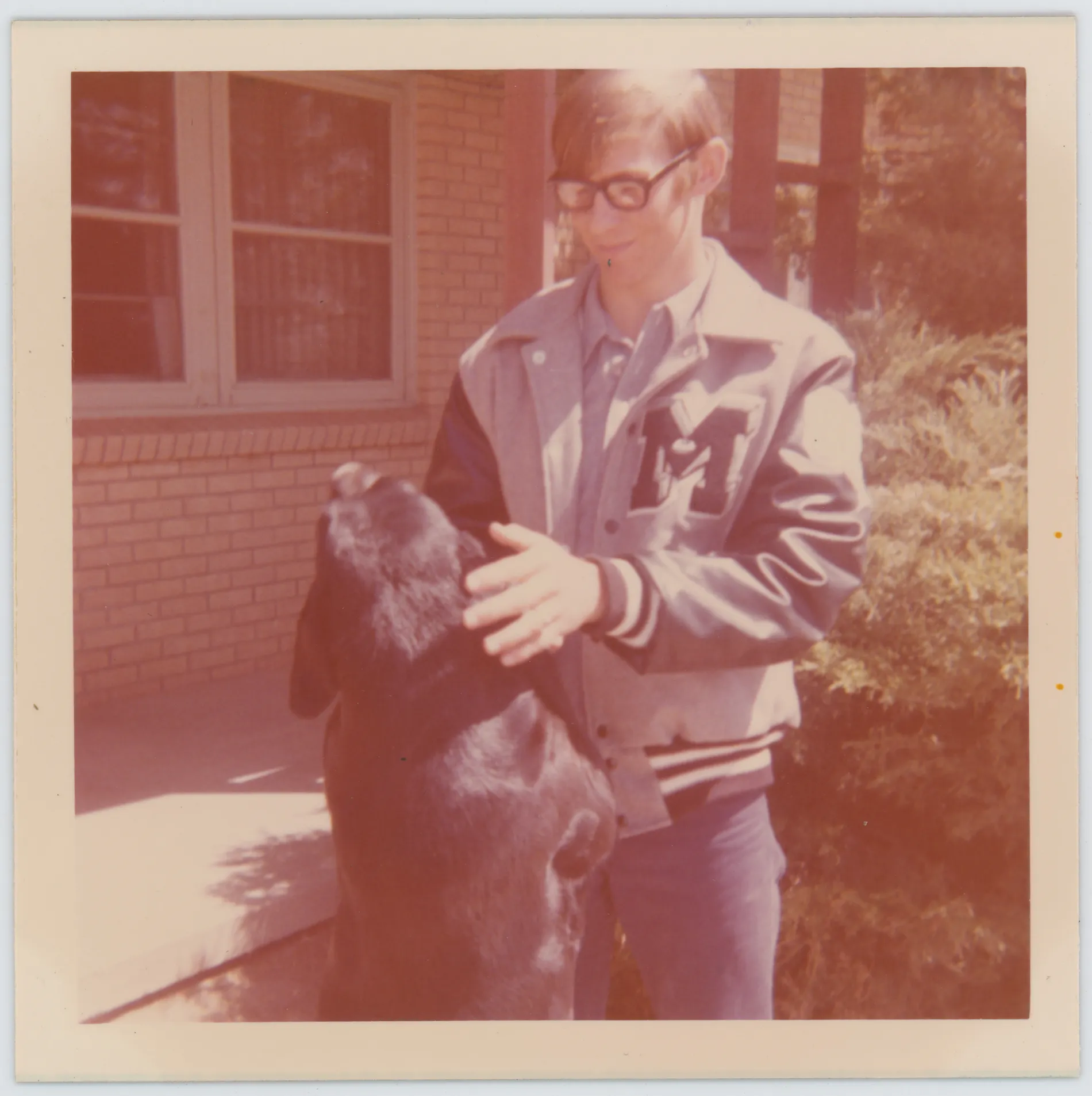 This photograph depicts Jack standing in front of his Lamb County home wearing his Muleshoe High School letterman jacket. A black labrador dog can be seen.