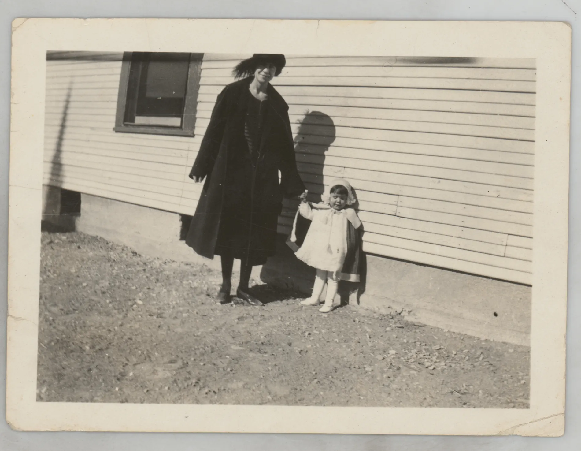 This photograph depicts Loveta McKinstry holding the hand of her daughter, Sammy, next to a structure.