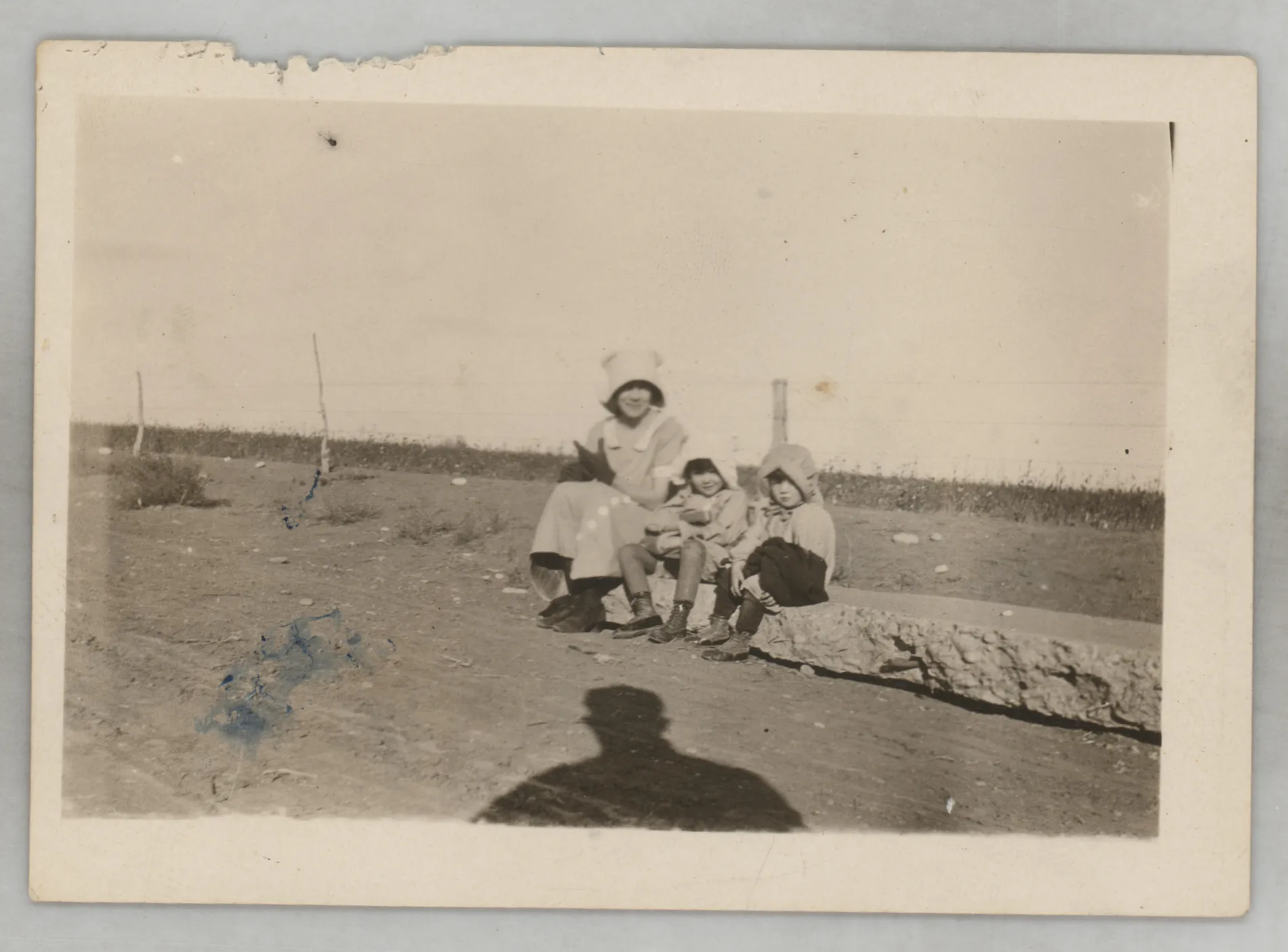 This photograph depicts Loveta, Sammy, and Jean McKinstry sitting on concrete next to a wire fence.