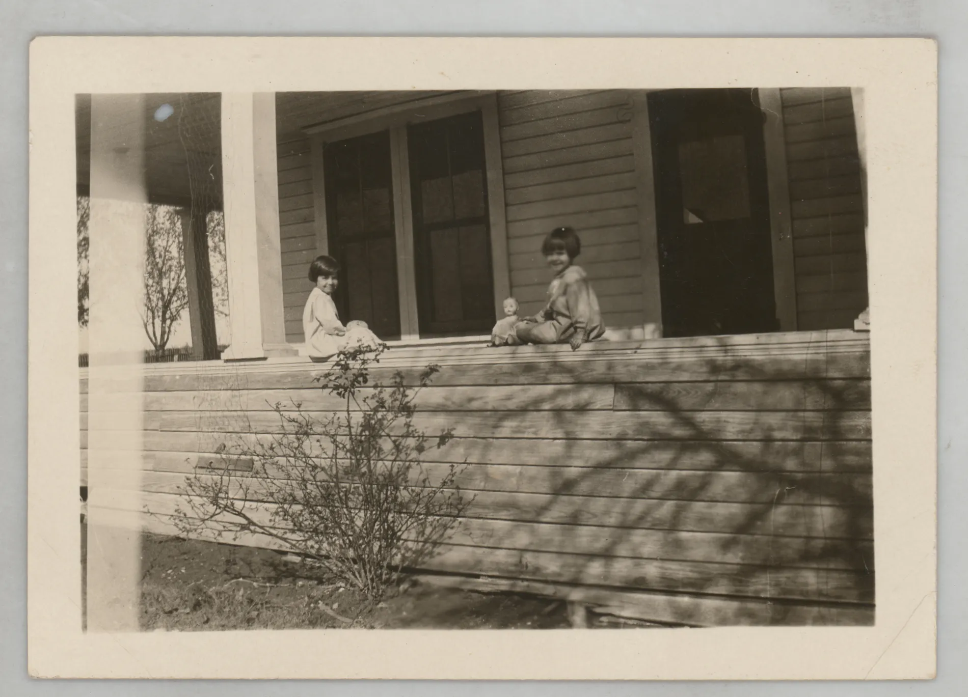 This photograph depicts Sammy McKinstry sitting on the porch playing with a doll. An unidentified girl is also on the porch.