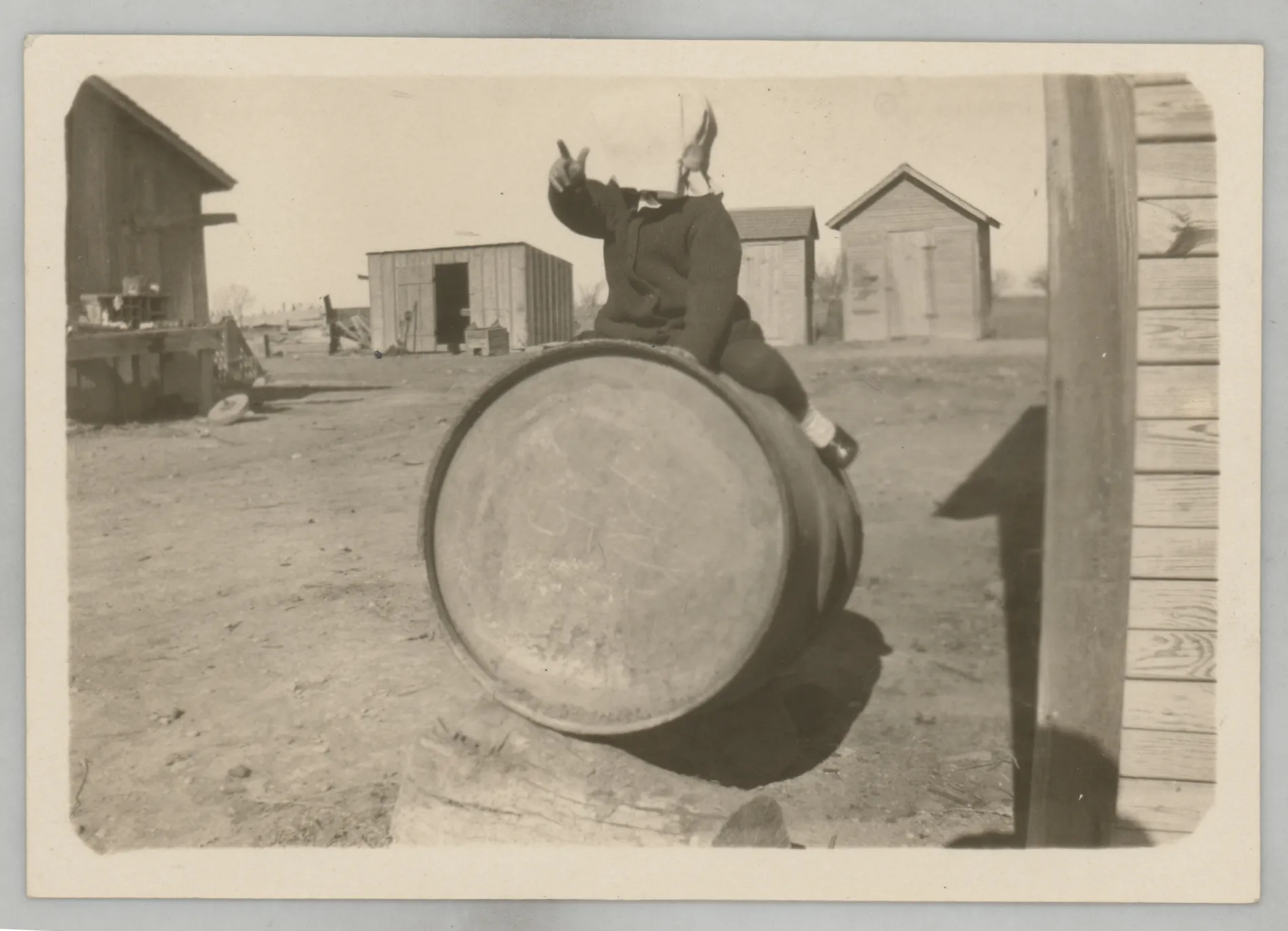 This photograph depicts Sammy McKinstry riding a barrel near several structures.