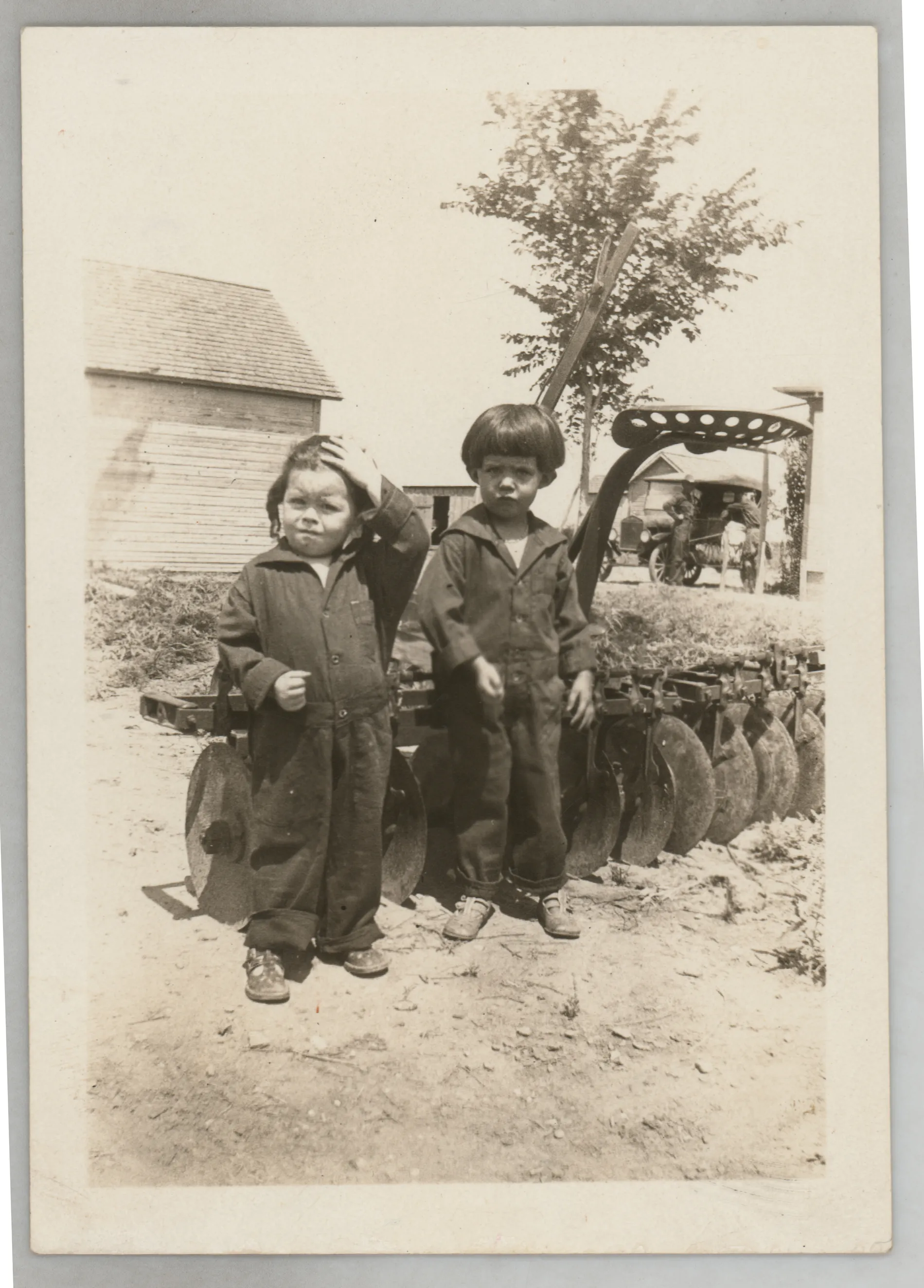 This photograph depicts Sammy McKinstry and cousin Camille Foster standing near farm equipment.