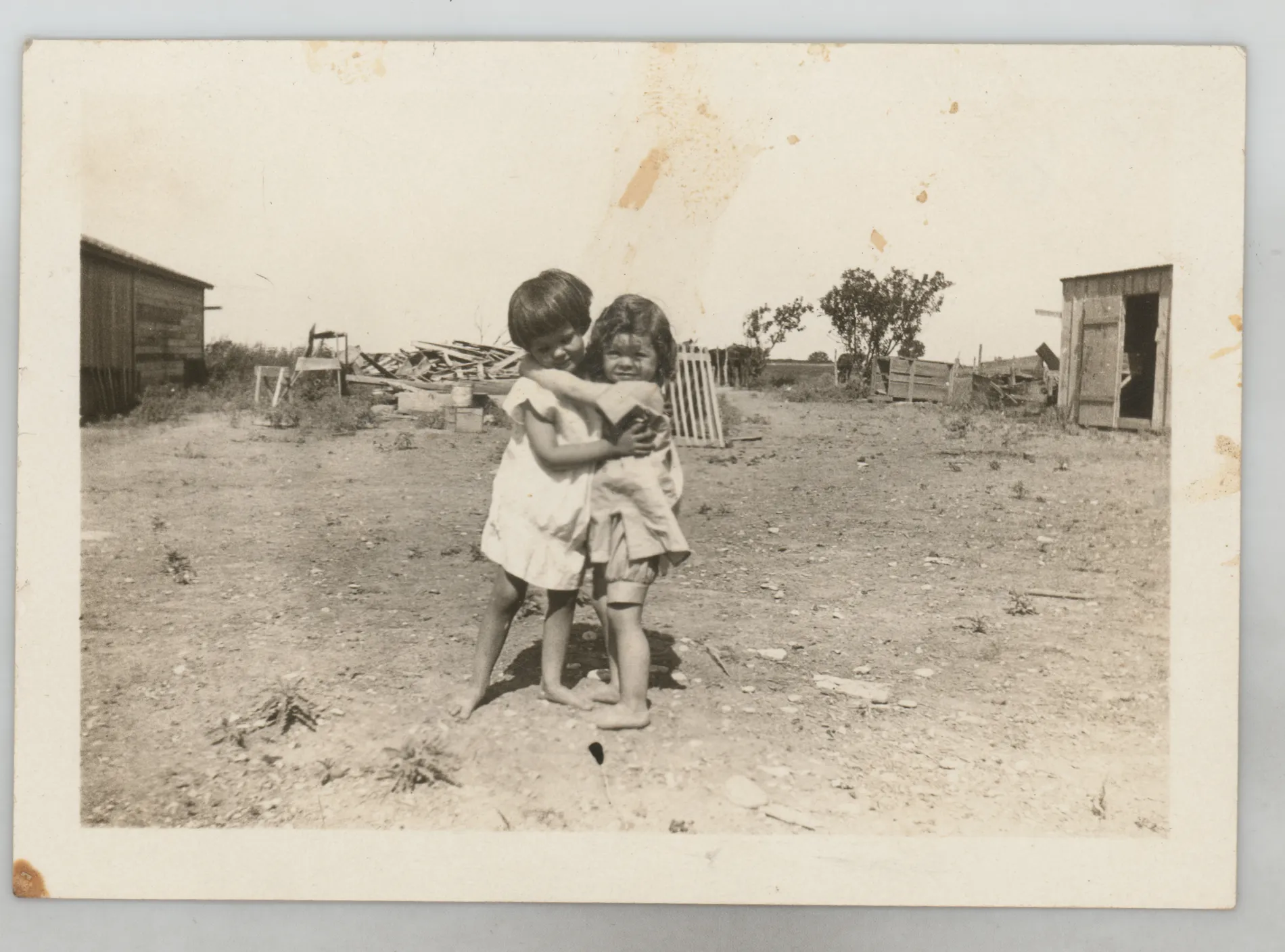 This photograph depicts Sammy McKinstry and cousin Camille Foster hugging near farm structures.