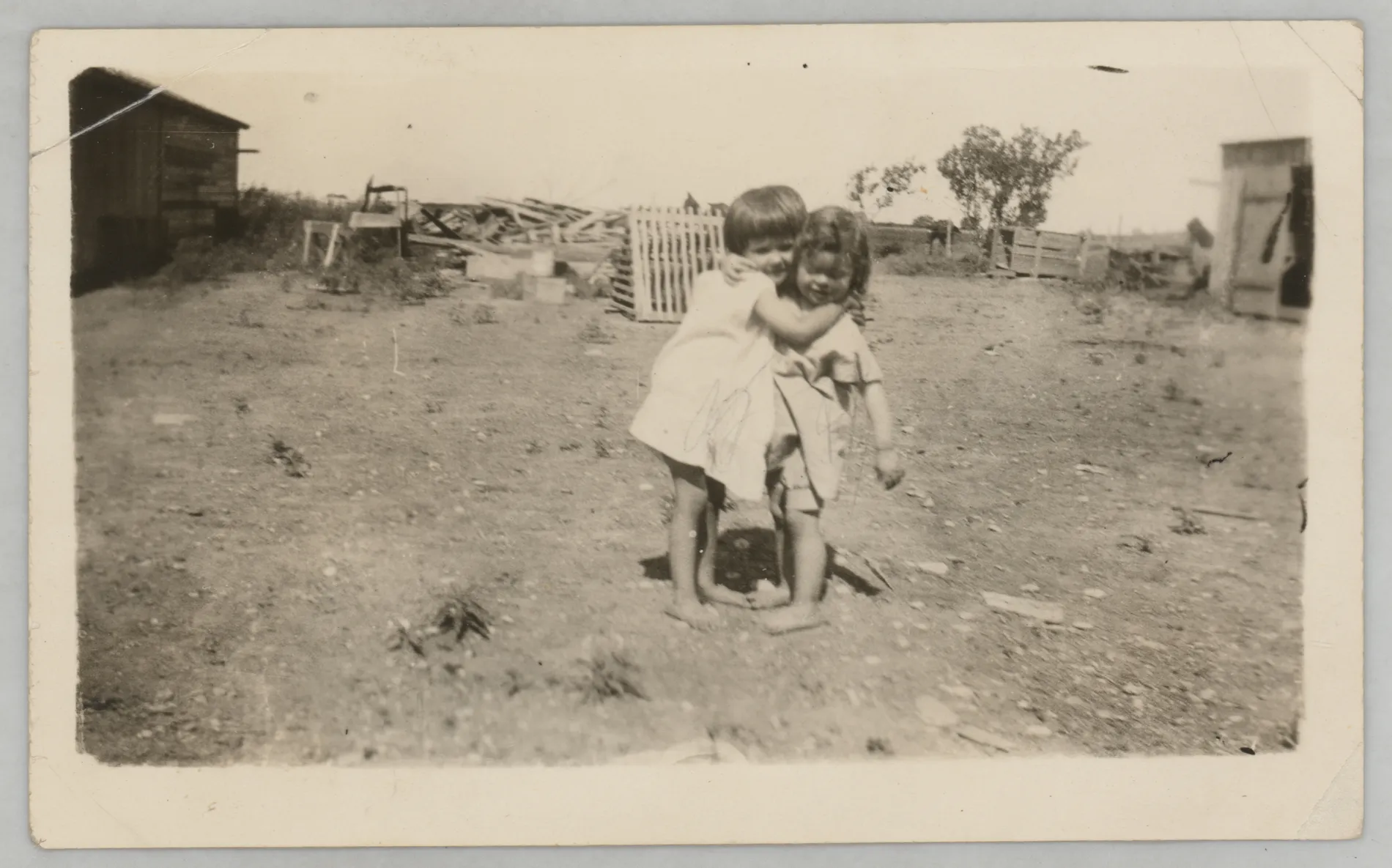 This photograph depicts Sammy McKinstry and cousin Camille Foster hugging near farm structures.