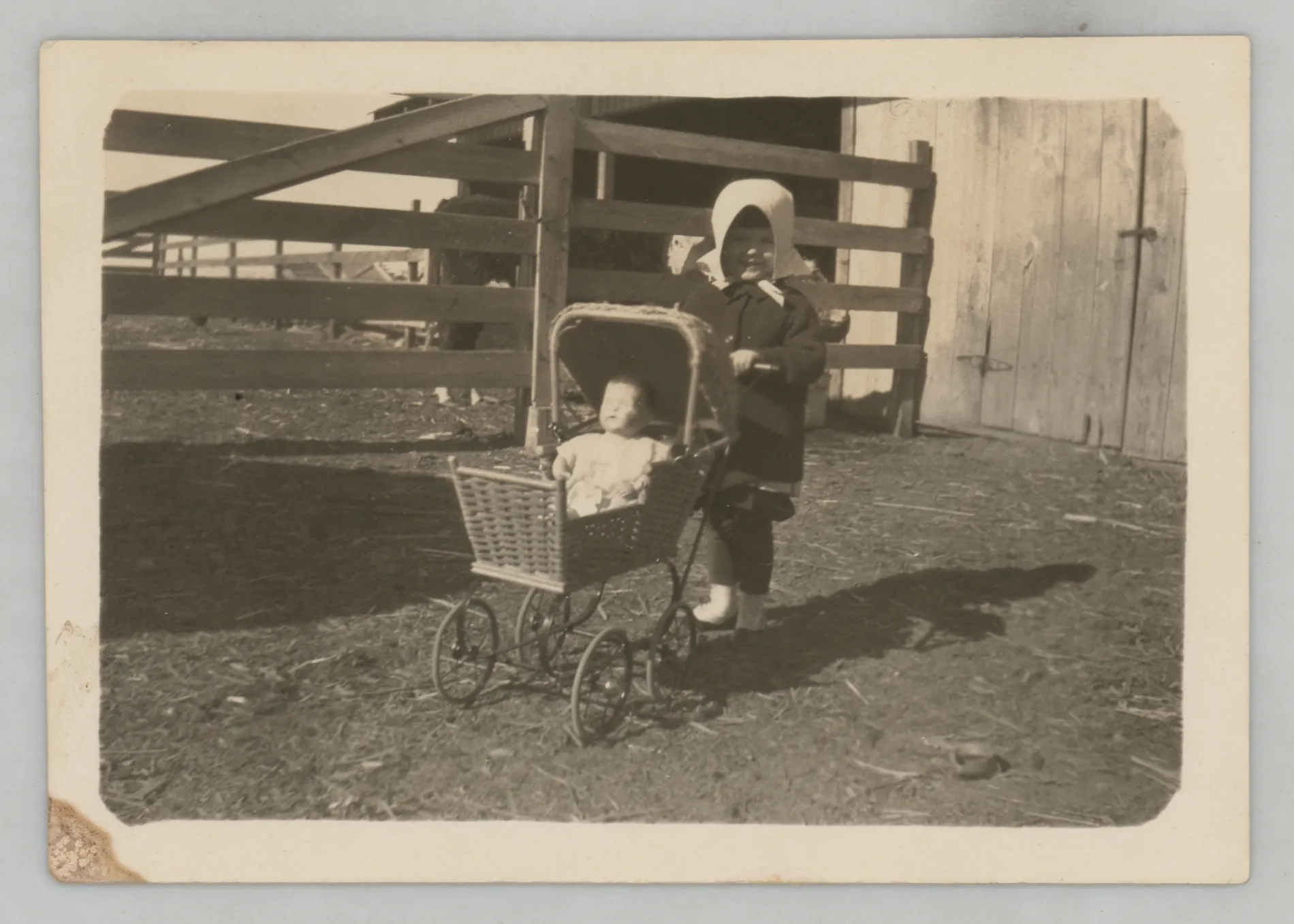 This photograph depicts Sammy next to a fence pushing a stroller with a doll in it. The doll's name was "Louise."