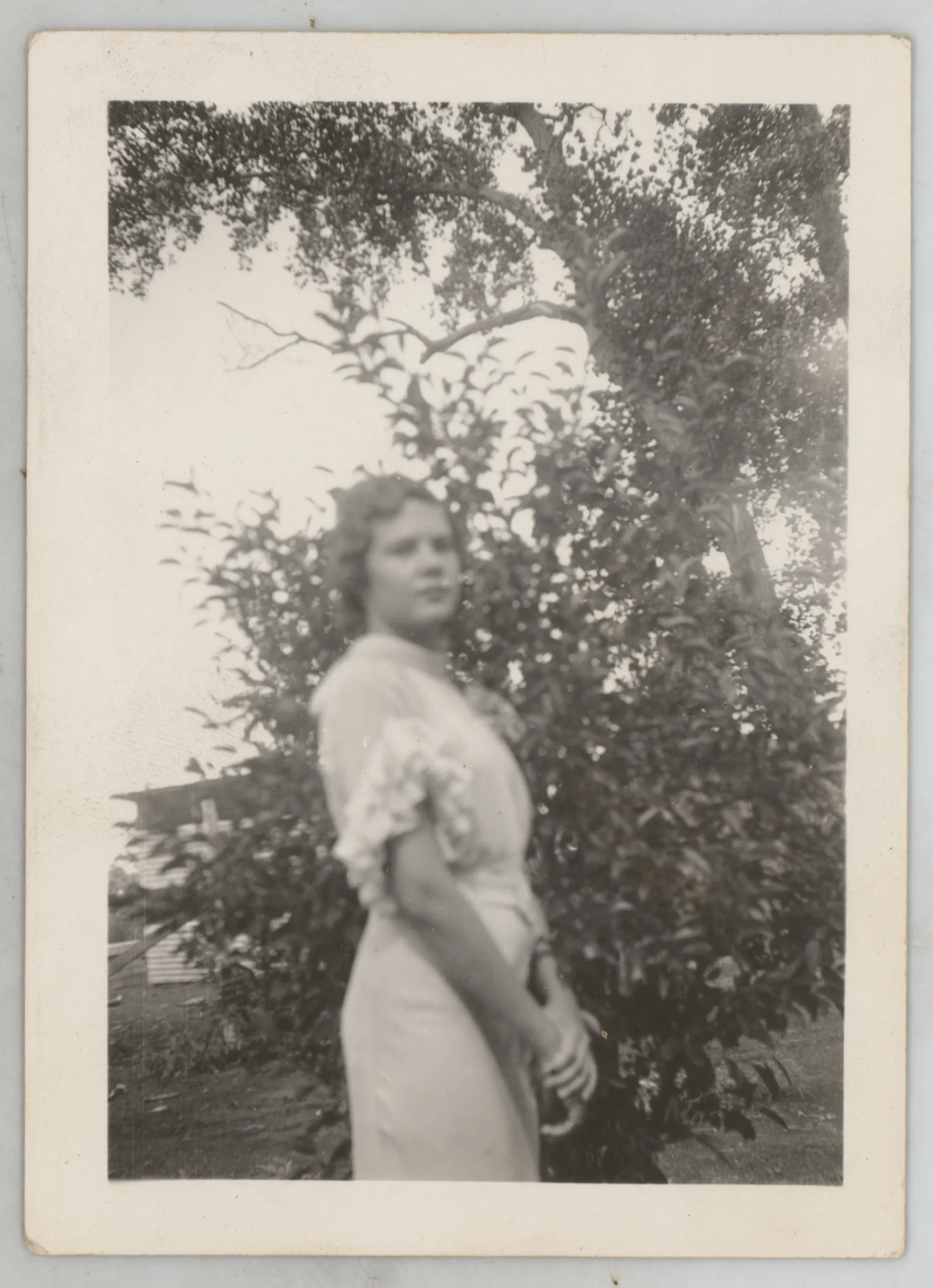 This photograph depicts Sammy McKinstry in a dress standing next to tree.