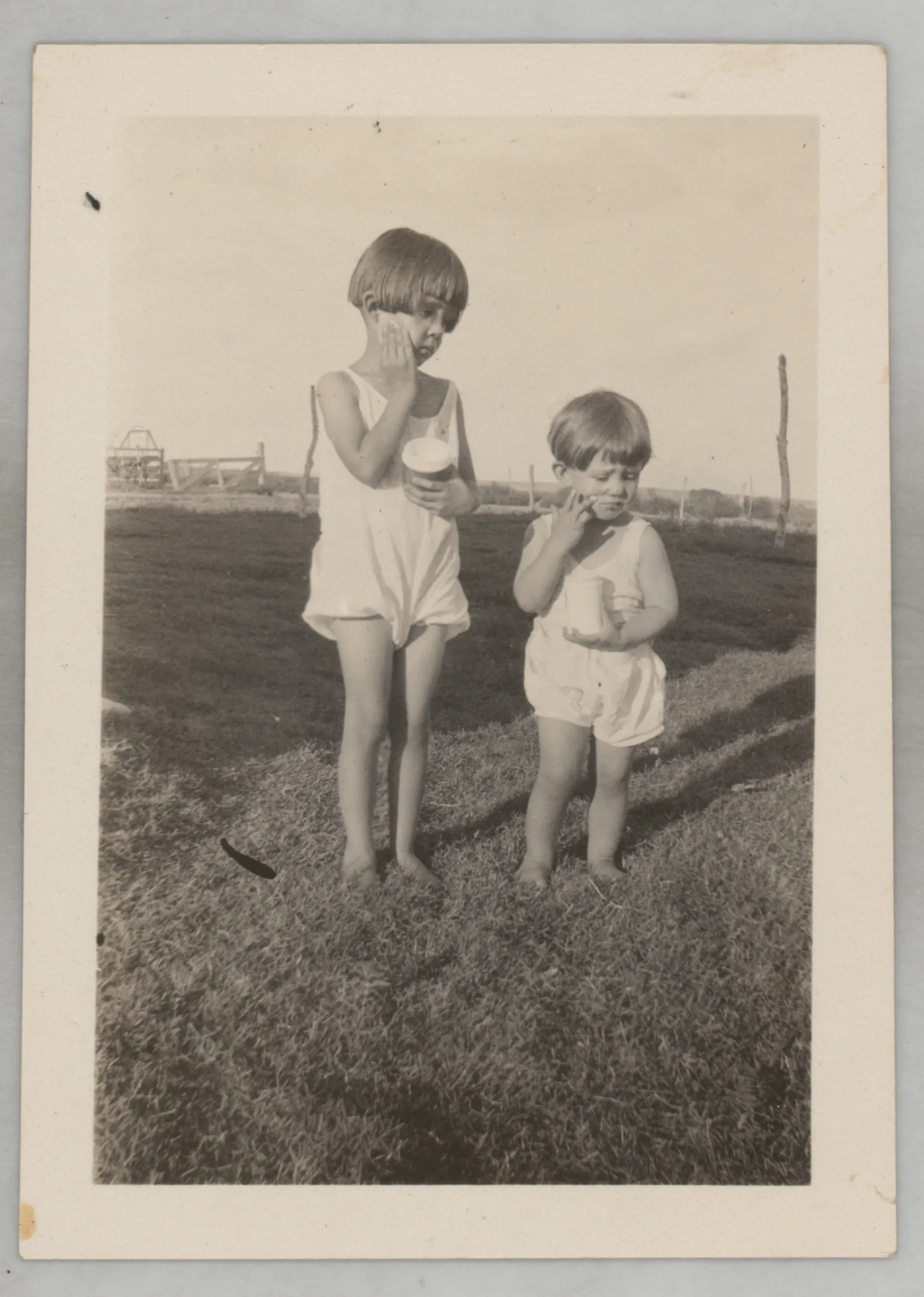 This photograph depicts Sammy and Jean McKinstry each holding jars. They are standing in the grass in a field with a fence in the background.