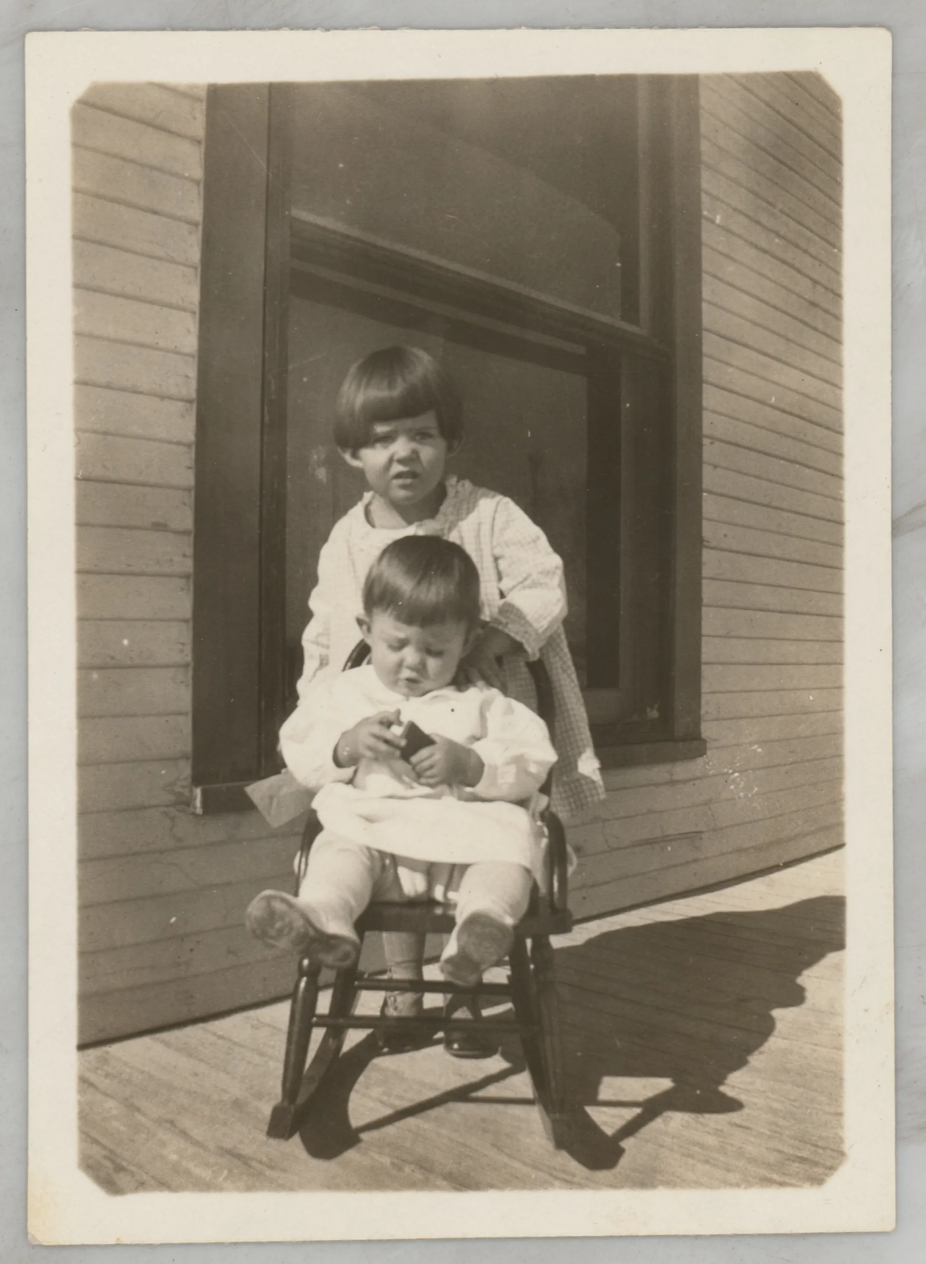 This photograph depicts Sammy and Jean McKinstry on a porch. Jean is in a rocking chair holding an item in her hands.