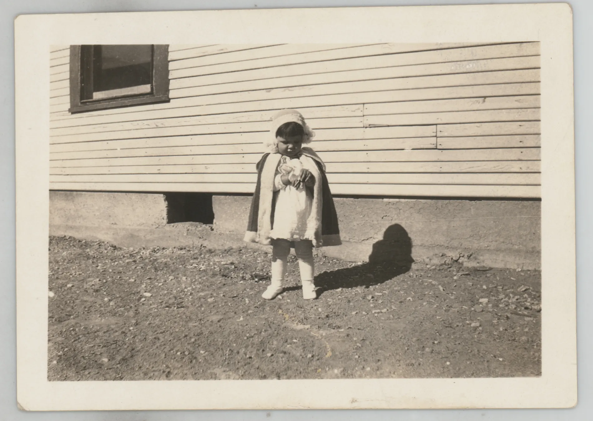 This photograph depicts Sammy McKinstry standing next to a house. She is wearing a hat, white shoes, and white leggings.
