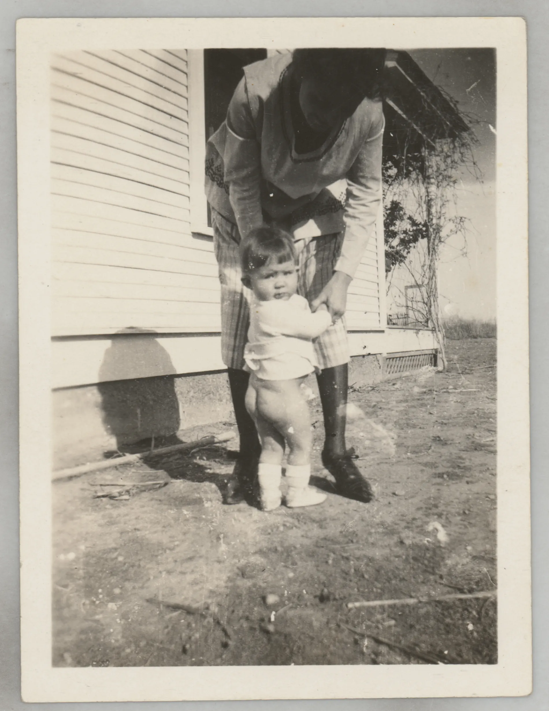 This photograph depicts Sammy McKinstry with her mother Loveta standing next to a house. Sammy has no pants on.