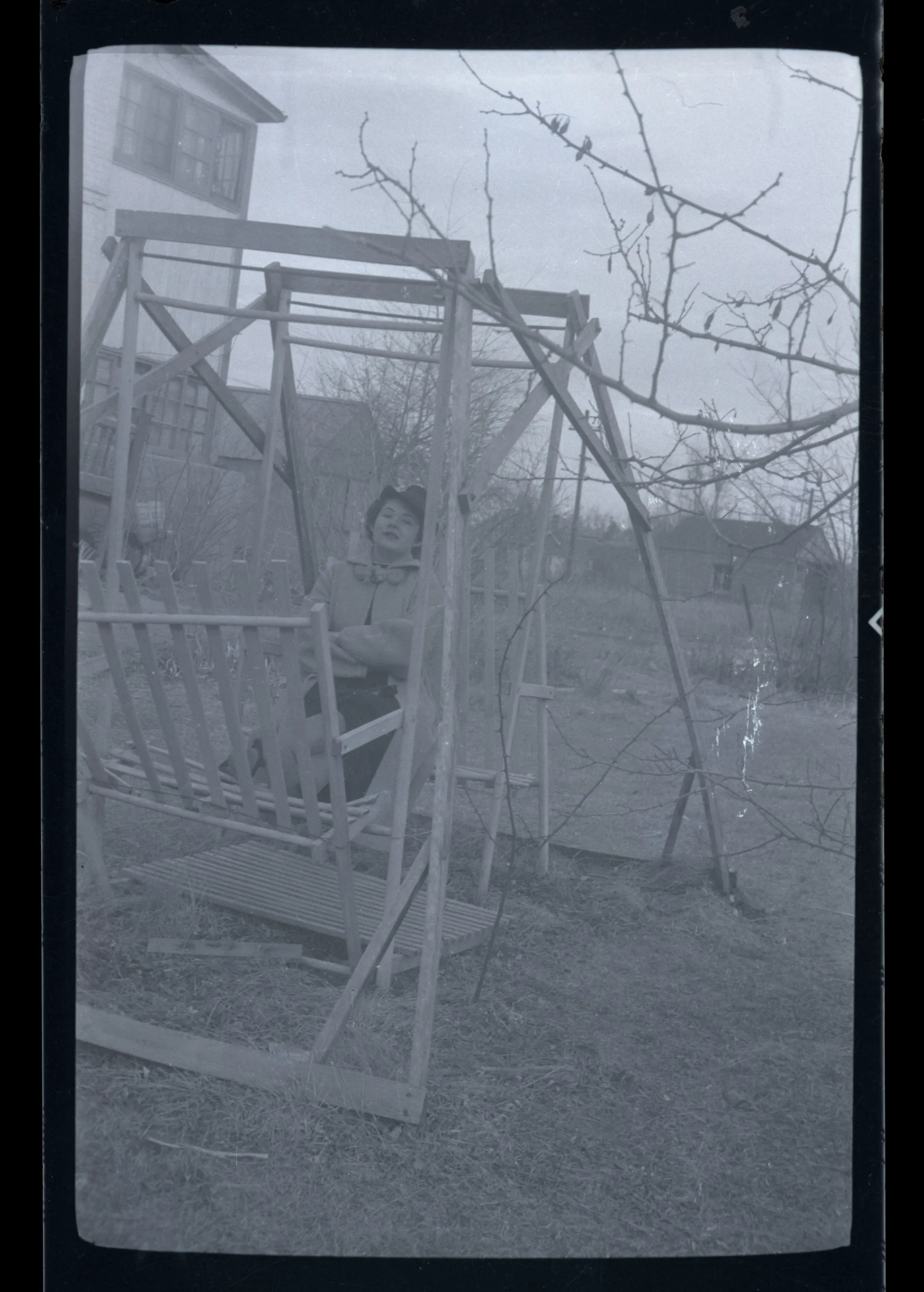 This photograph depicts Sammy McKinstry sitting on a swing. She is wearing a dark-colored hat. This photograph appears similar in production to other photos potentially from her time at Colorado Women's College.