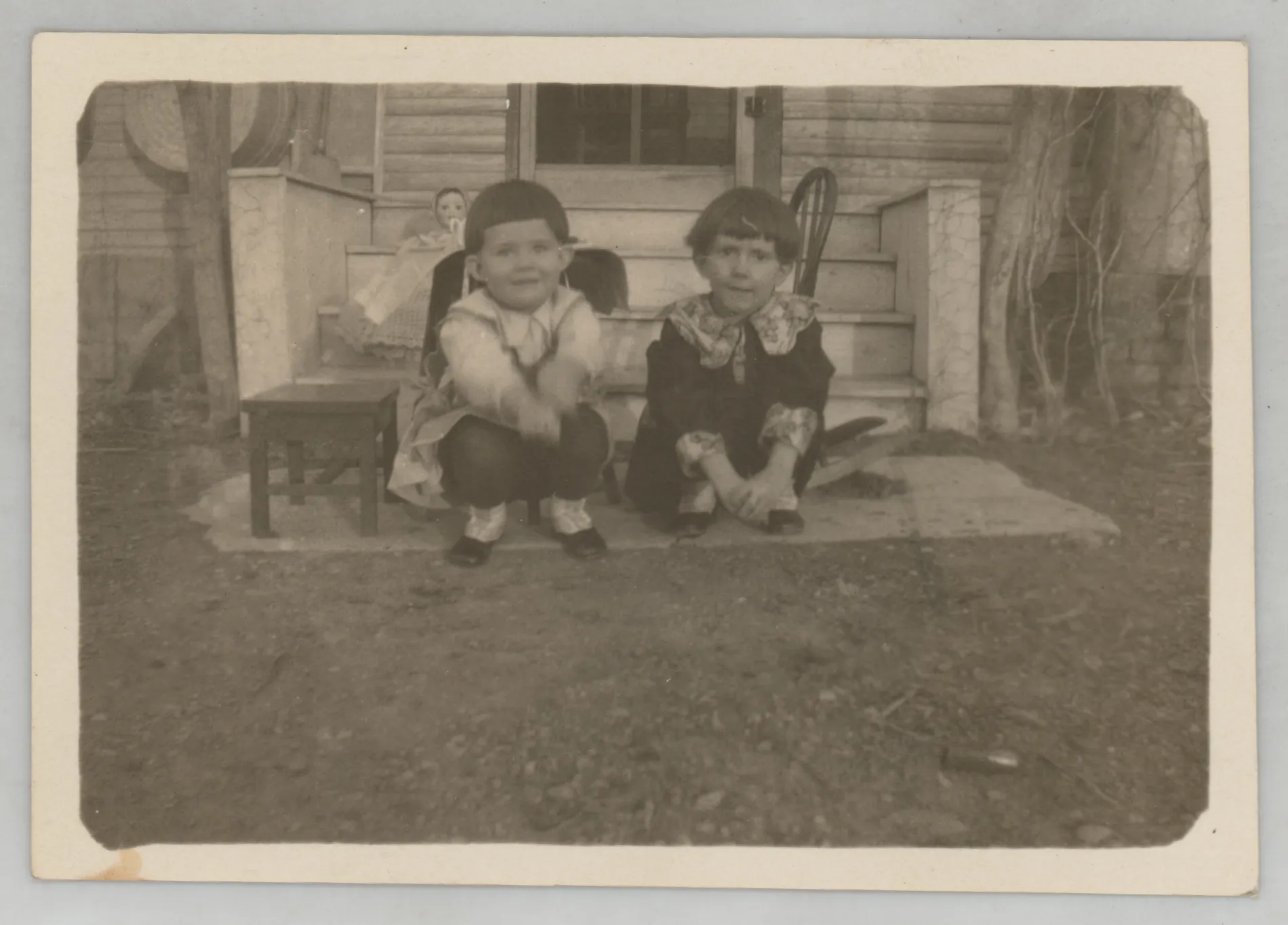 This photograph depicts Sammy McKinstry and her cousin Sara Beth West kneeling next to a porch.