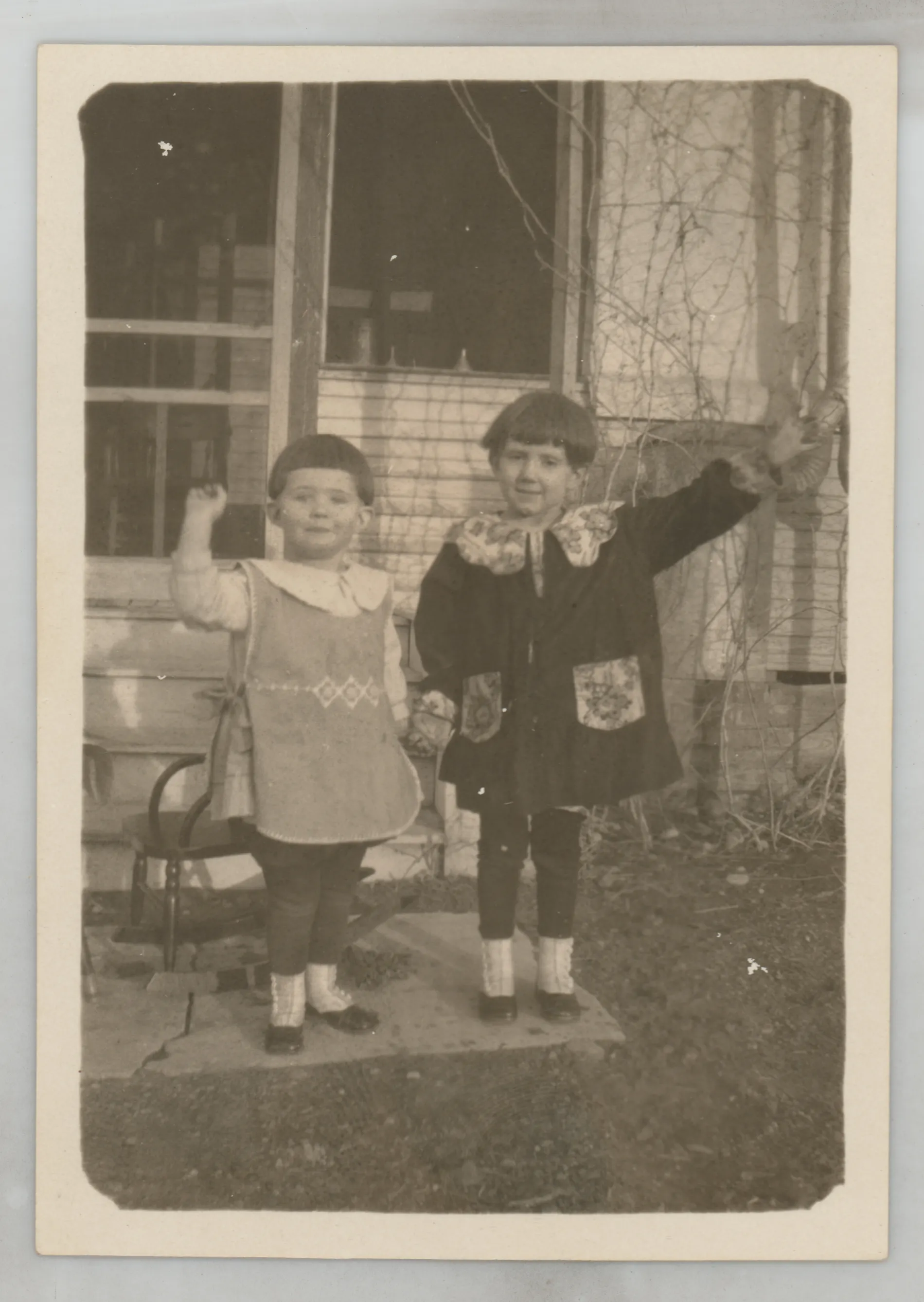 This photograph depicts Sammy McKinstry and her cousin Sara Beth West waving at the camera while standing next to a house.