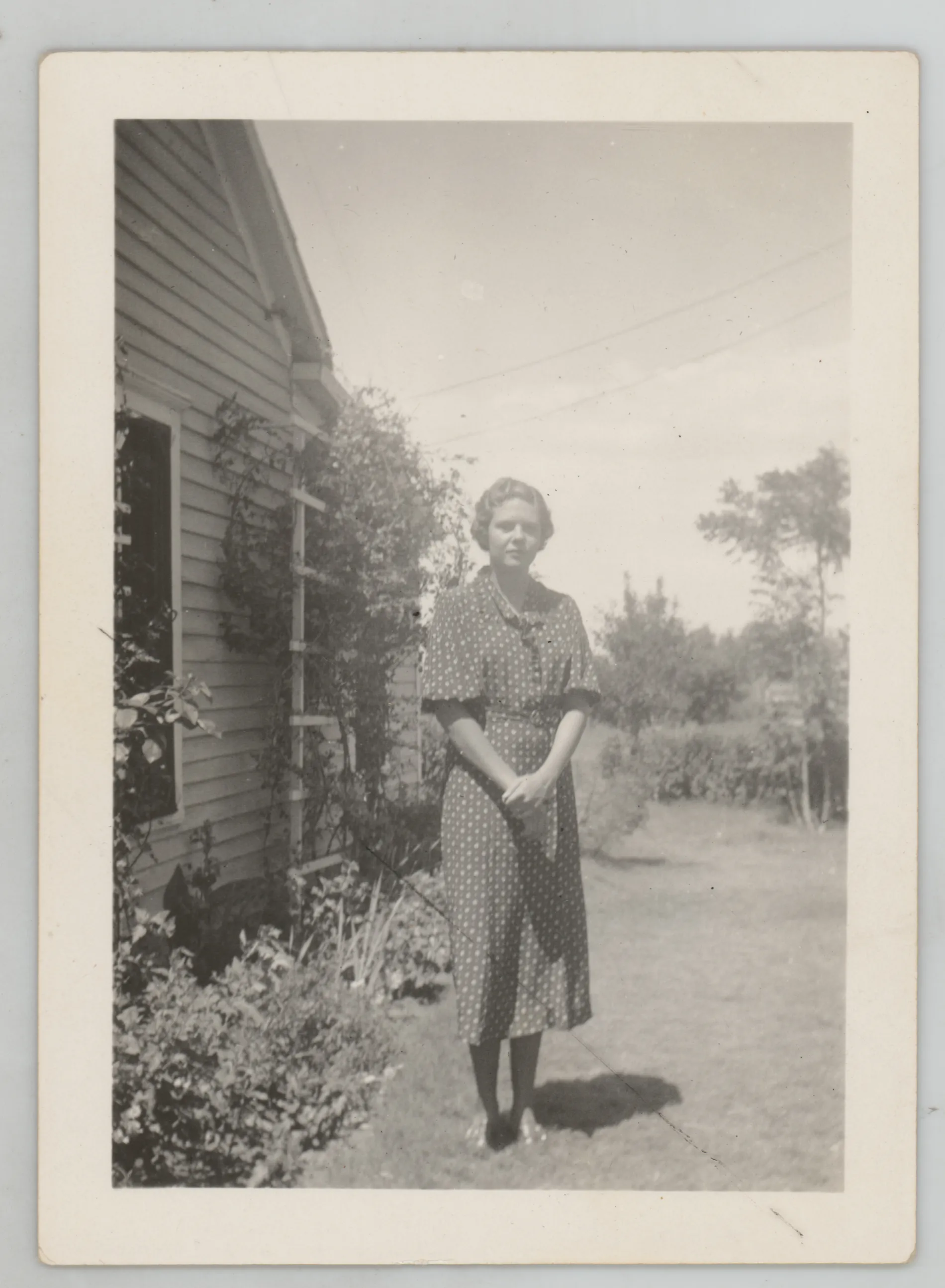 This photograph depicts Sammy McKinstry standing next to a house in a spotted dress.