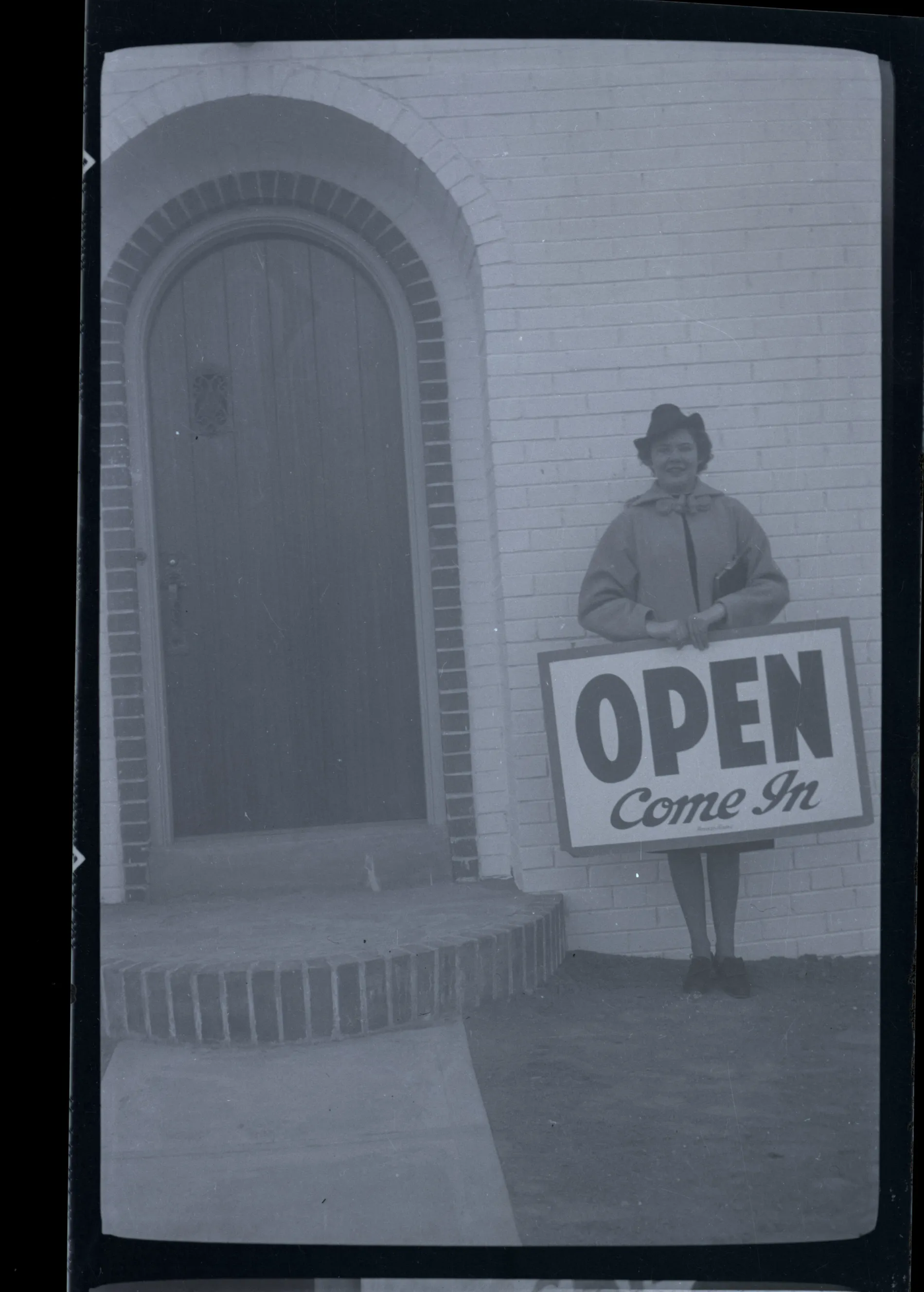 This photograph depicts Sammy McKinstry holding a sign that says "Open, Come In." This photogrpah may be from Sammy's time in Denver at Colorado Women's College.