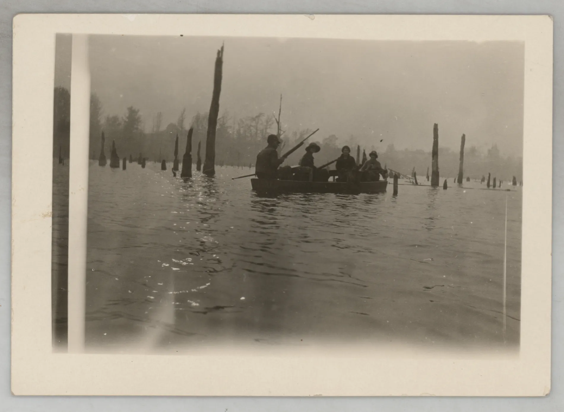 This photograph depicts four people in a boat. None of the individuals are identifiable, but each one appears to be holding a firearm.