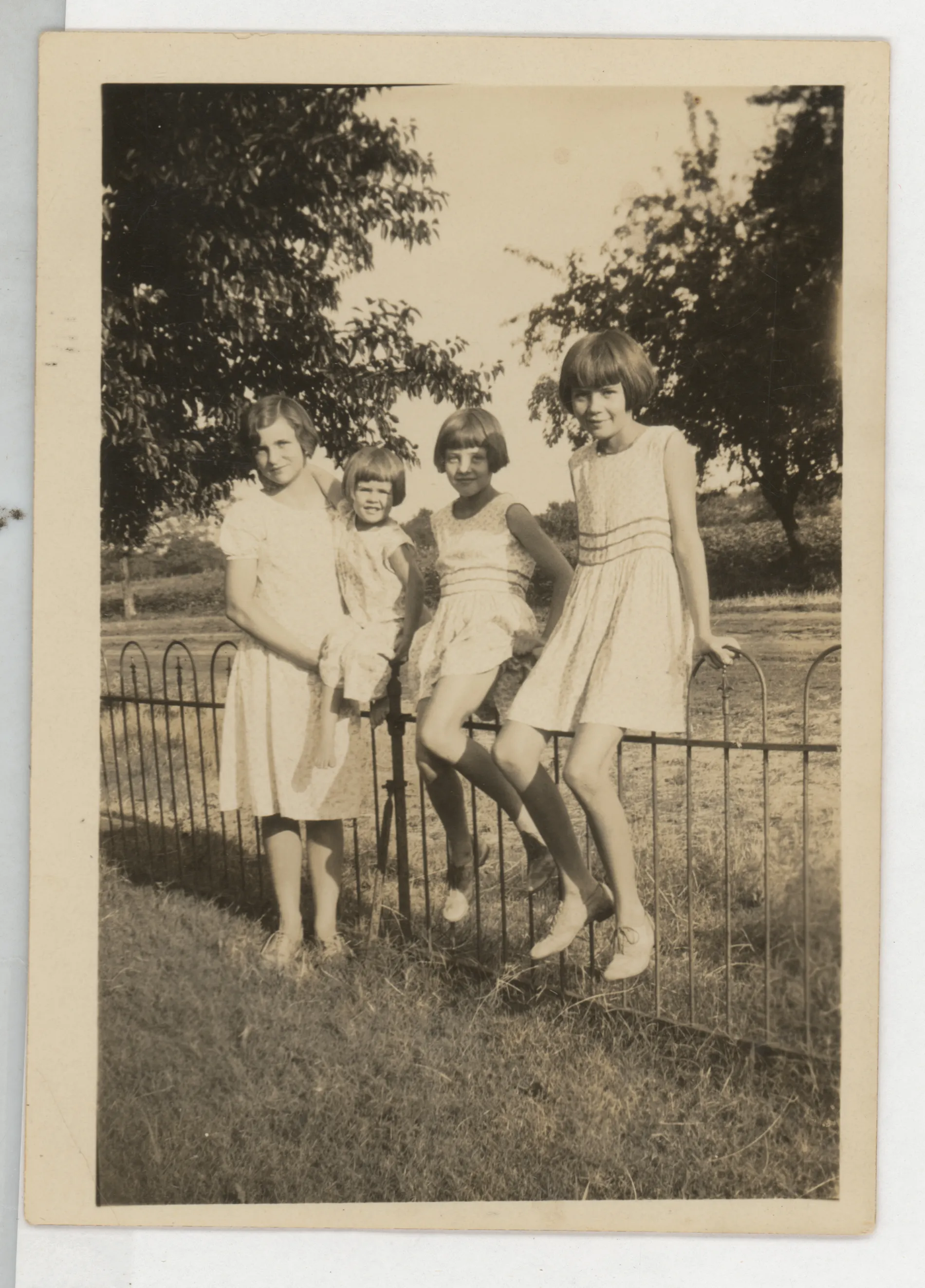 This photograph depicts the children of Sam and Loveta McKinstry, Sammy, Jean, and Mildred, and a cousin Ruth at Aunt Nannie's home in Jacobia, Texas. The McKinstrys are sitting on the fence, while Ruth is standing to the left.