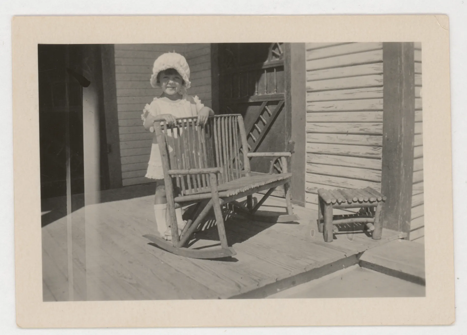 This photoraph depicts Jean McKinstry standing on a porch next to a rocking chair.