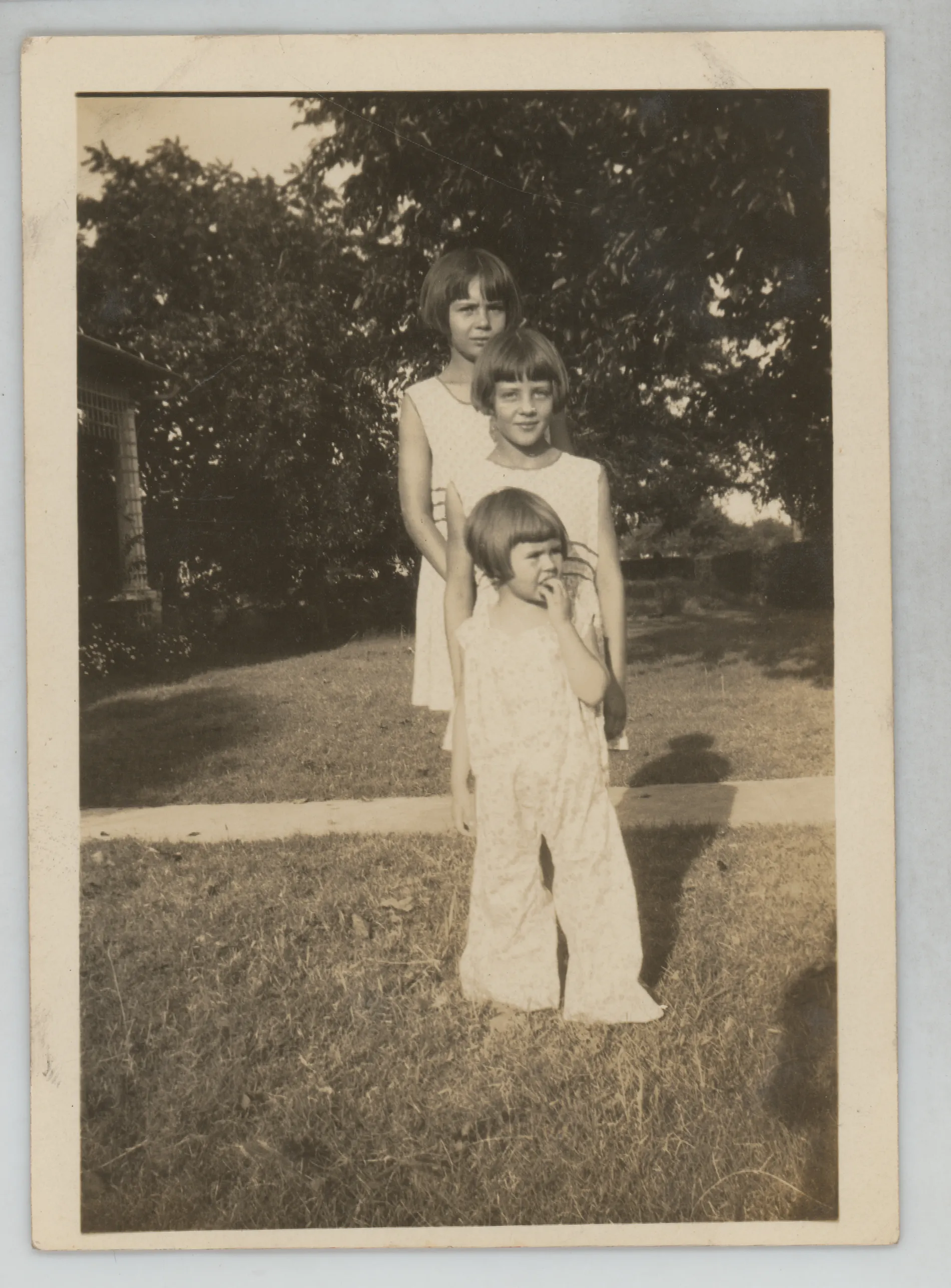 This photograph depicts Sammy, Jean, and Mildred McKinstry standing one in front of another in the yard of C.E. and Nannie Girdner in Jacobia, Texas.