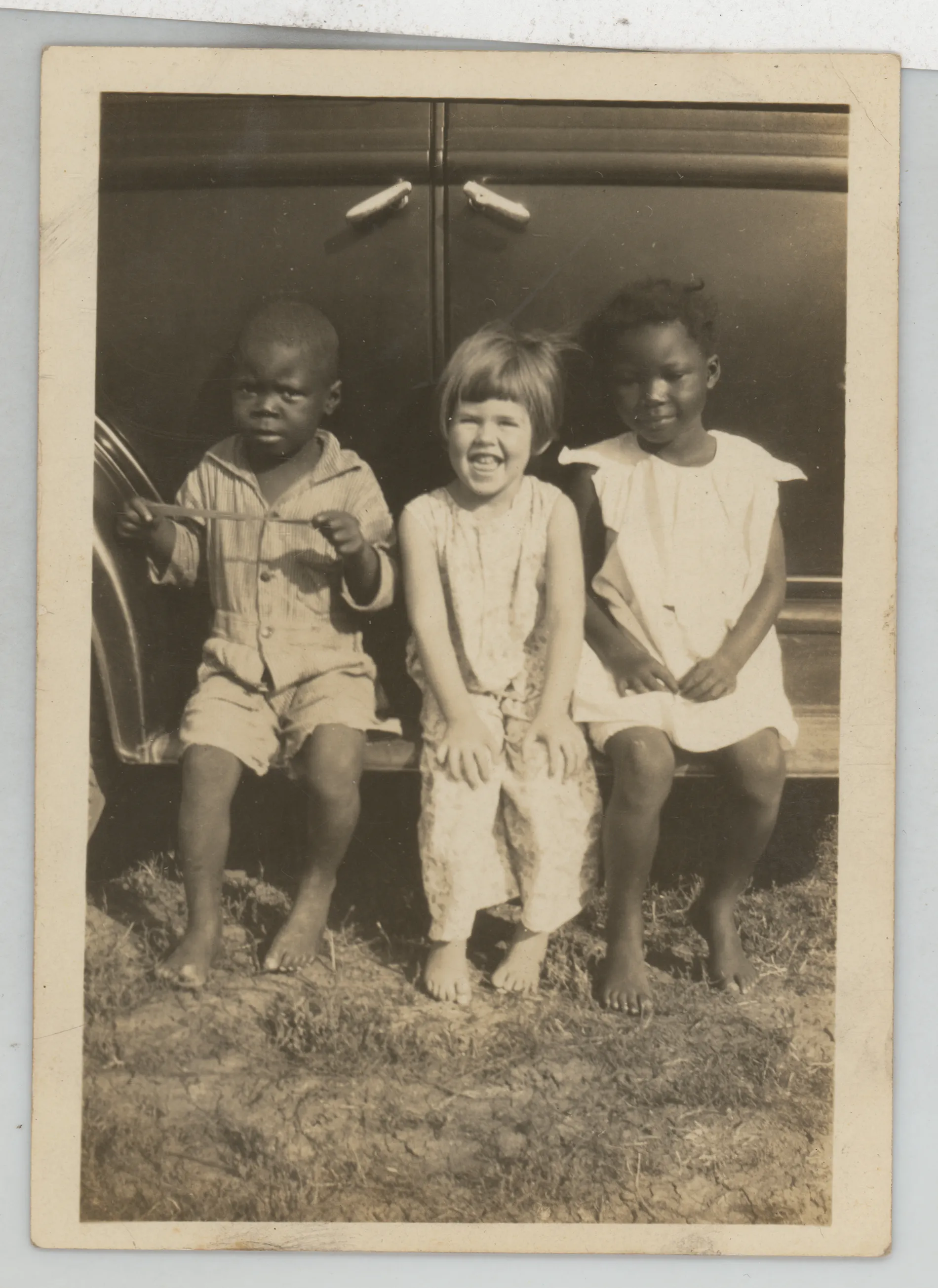 This photograph depicts Mildred McKinstry sitting on the step of a vehicle between two unidentified African American children. 