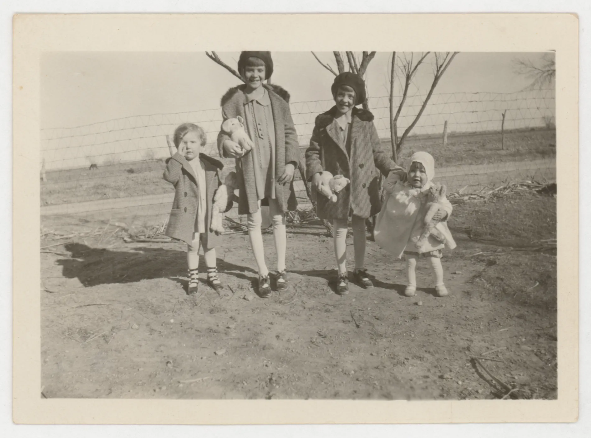 This photograph depicts Peggy, Sammy, Jean, and Mildred McKinstry in 1929. They are stanindg in front of a road and a fence.