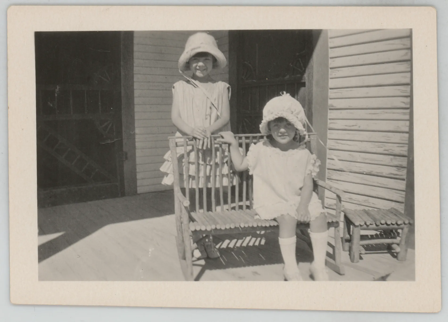 This photograph depicts Sammy and Jean McKinstry on a porch. Sammy is standing behind the chair, and Jean is sitting on the chair.