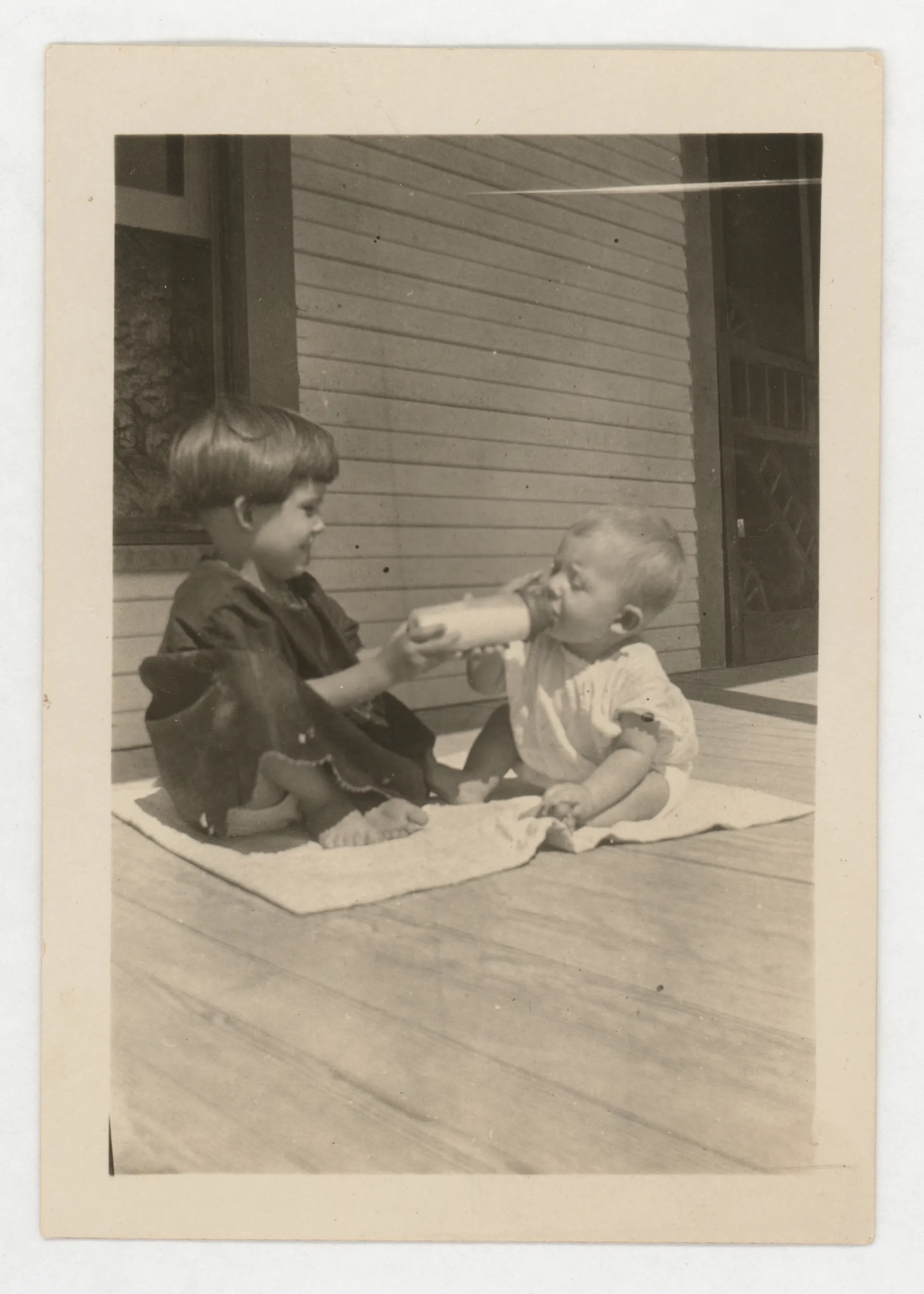 This photograph depicts Sammy and Jean McKinstry on a porch. Sammy is helping Jean with a bottle.