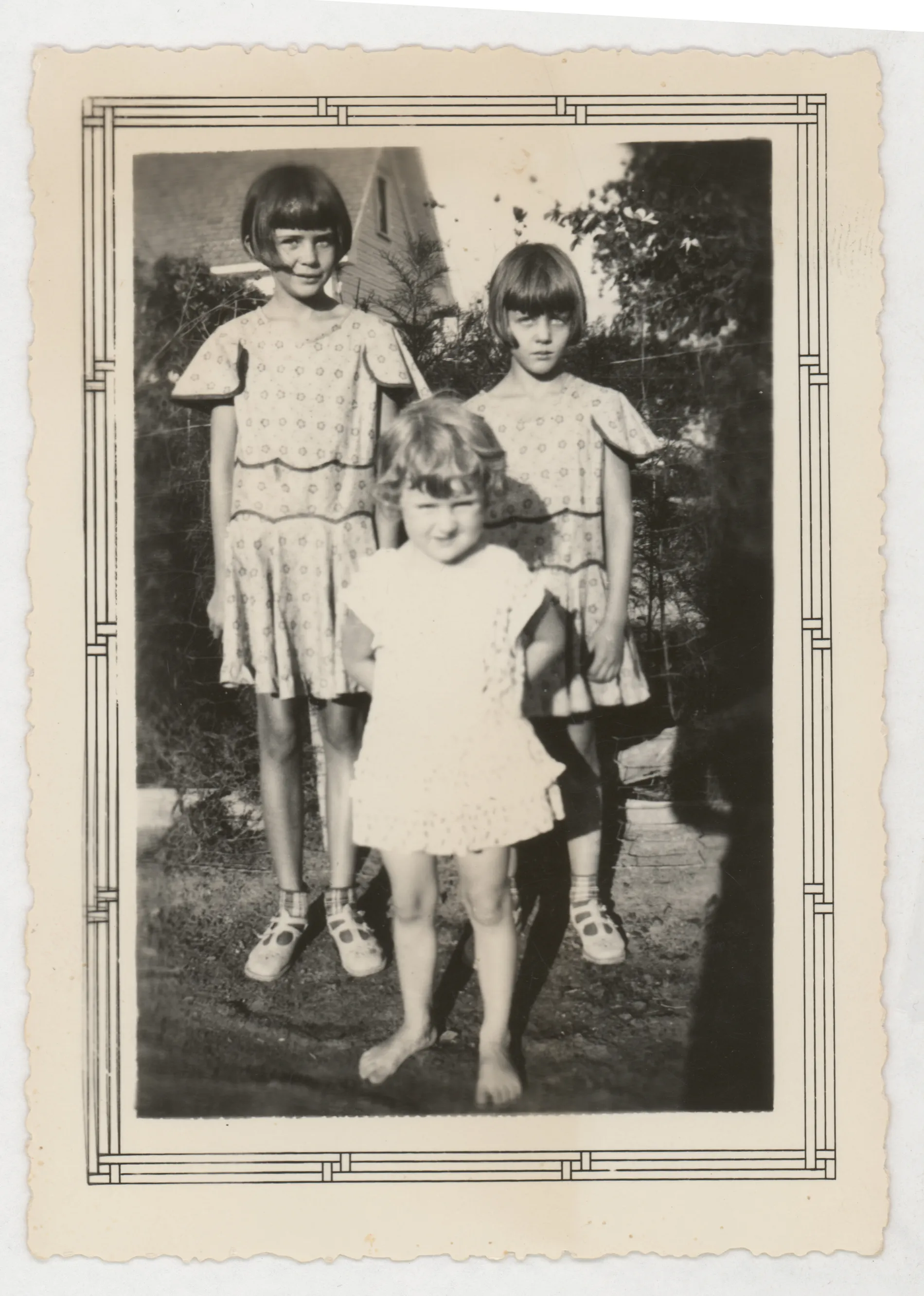 This photograph depicts Sammy, Jean, and Peggy McKinstry standing in front of a fence and some bushes.