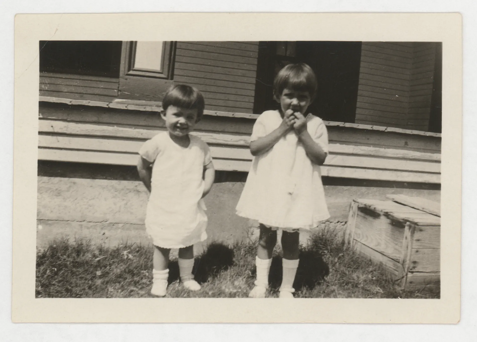 This photograph depicts Sammy McKinstry and her cousin Sara Beth West. The photograph depicts them standing in front of a porch.