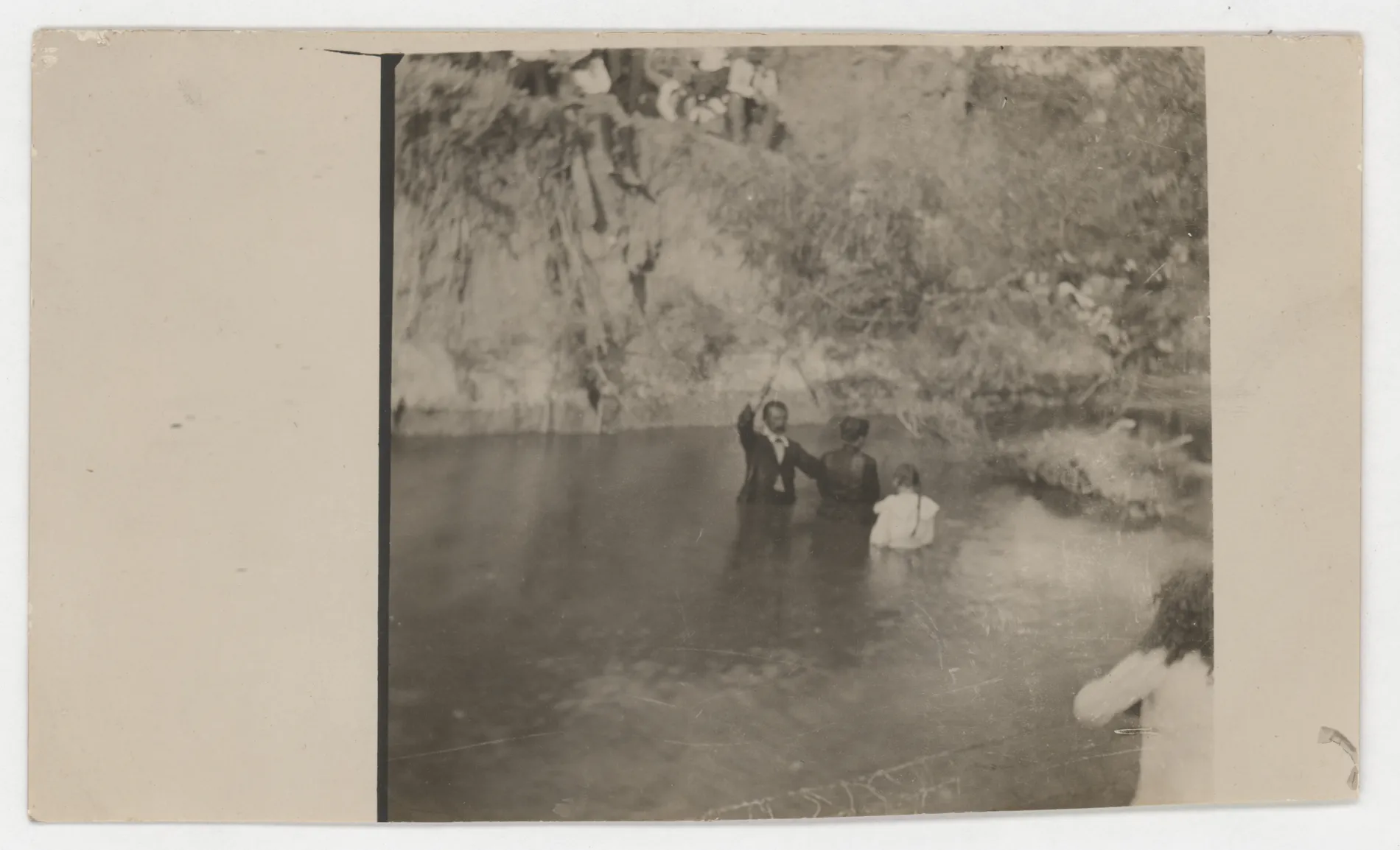 This photograph depicts a baptism in a pool likely in Jacobia, Texas. There are three main figures in the center of the image and then several people at the top and at the bottom of the picture. No one is identified.
