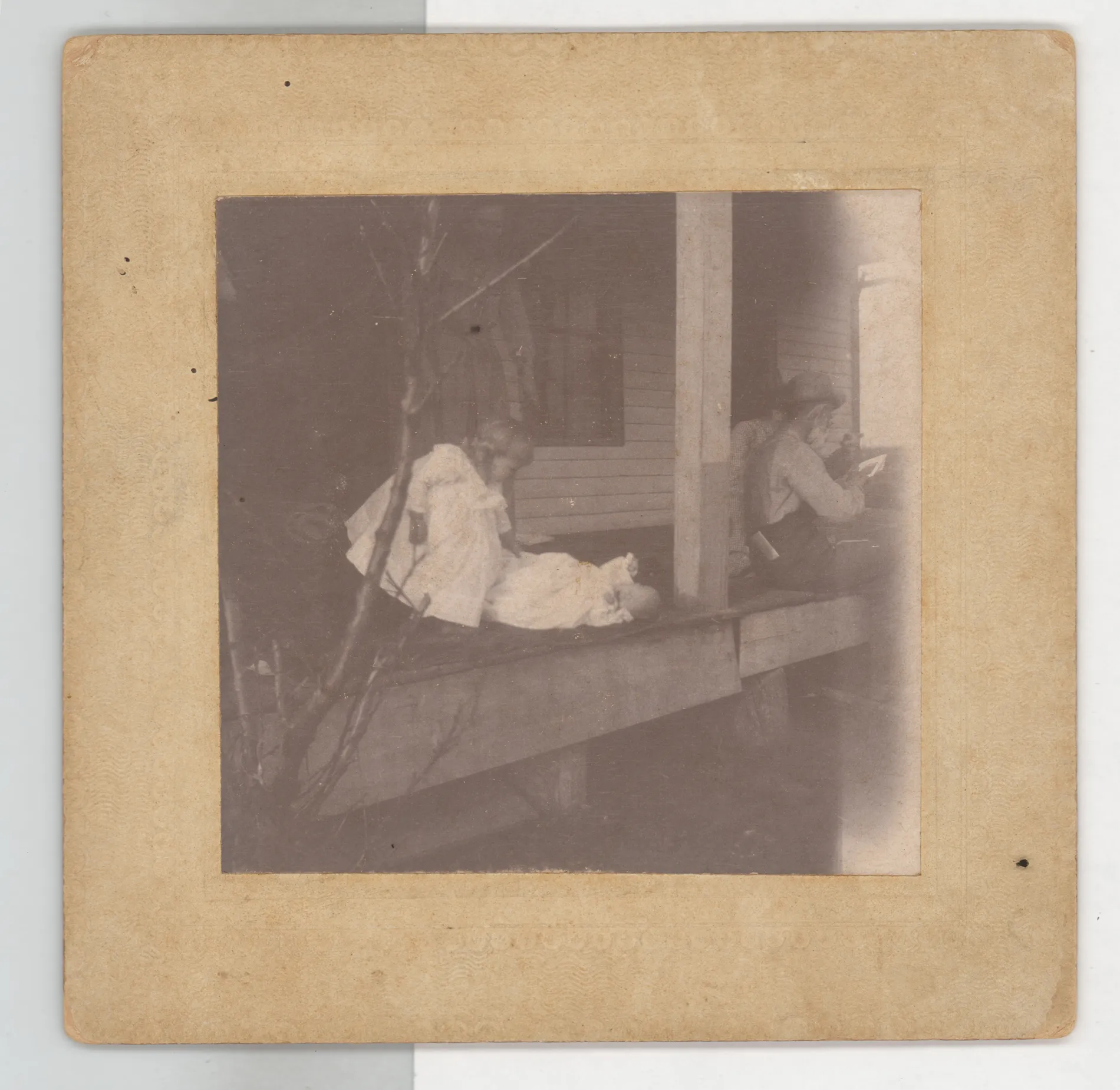 This photograph depicts Vena Girdner and Austin Girdner on a porch. Another man, identified as Mr. Prather, sits on the right side of the porch.