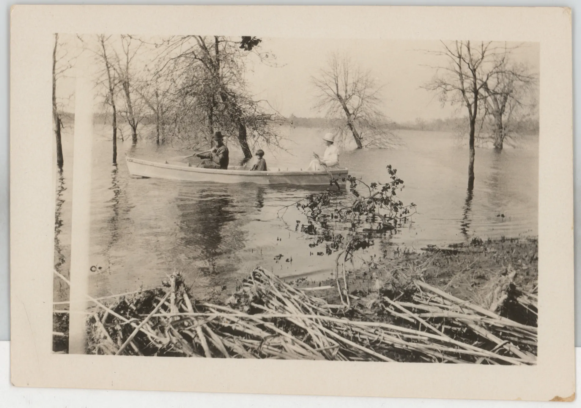 This is a photograph of three people in a boat during a flood at Jacobia. The inscription on the verso does not offer a potential date or potential figures in the boat. The hairstyle matches that of Sammy and Jean McKinstry in the early to mid 1920s, but they never lived at Jacobia. Such hairstyles would not have been on children when the Swanns lived at Jacobia. I believe this is from a later flood. This photograph may depict Sam, Loveta, and Sammy McKinstry.
