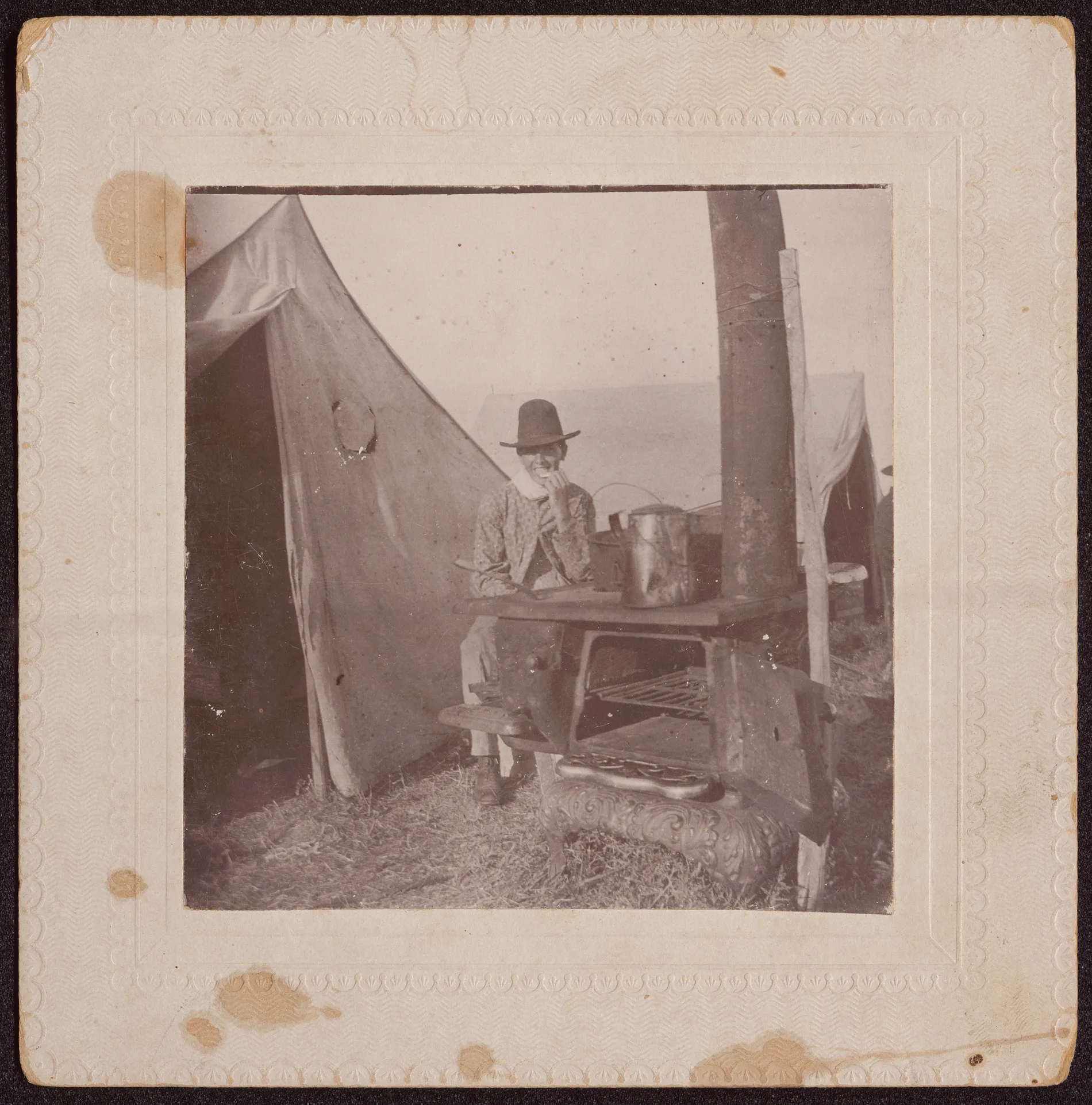 This photograph depicts cook Claude Lovell sitting next to a stove on one of the Austin Swann threshing trips to Oklahoma in 1900 and 1901.
