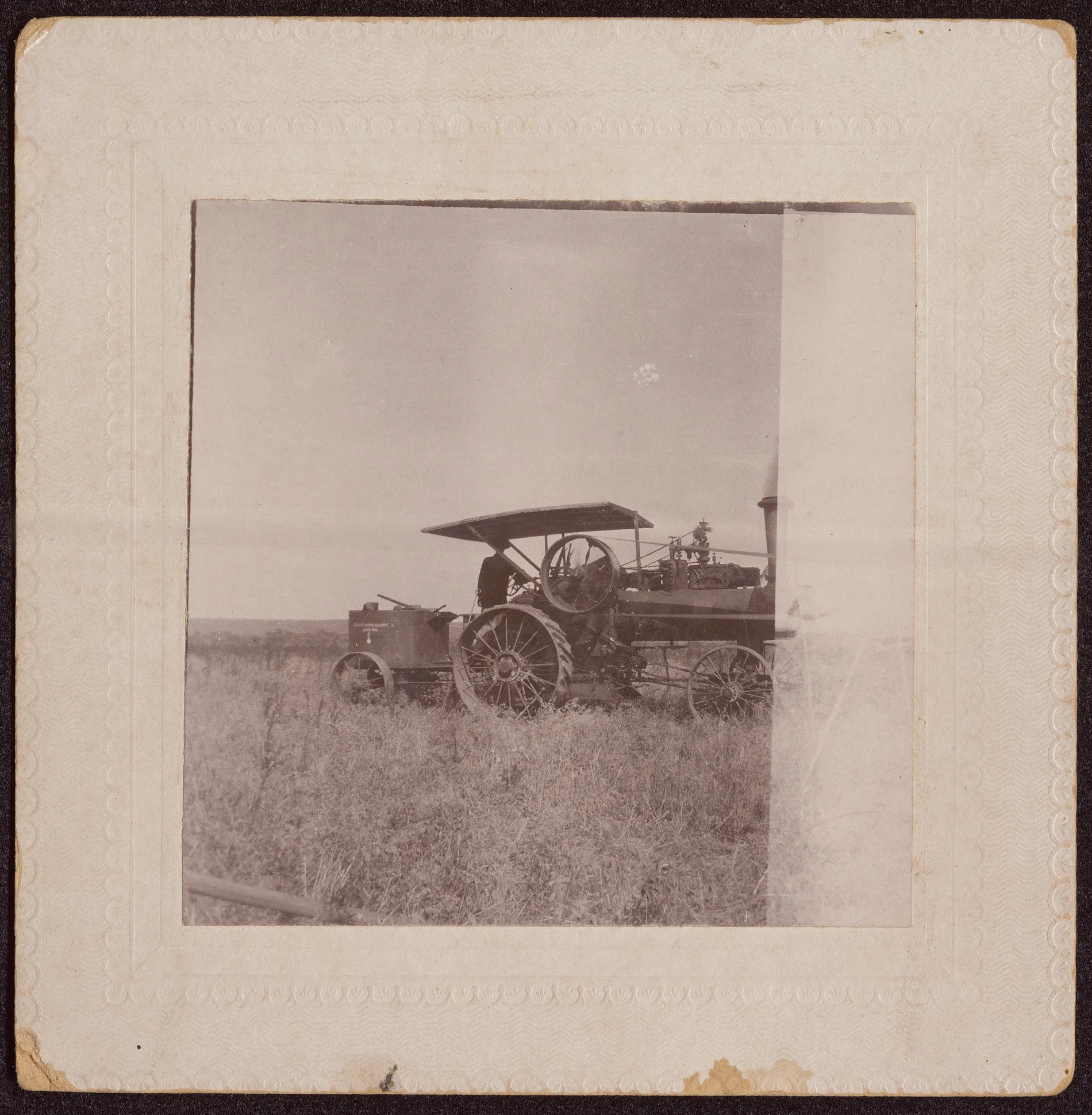 This photograph depicts a man, likely Austin Swann, operating a steam engine in a field. The right side of the photograph is faded and less clear than the rest.