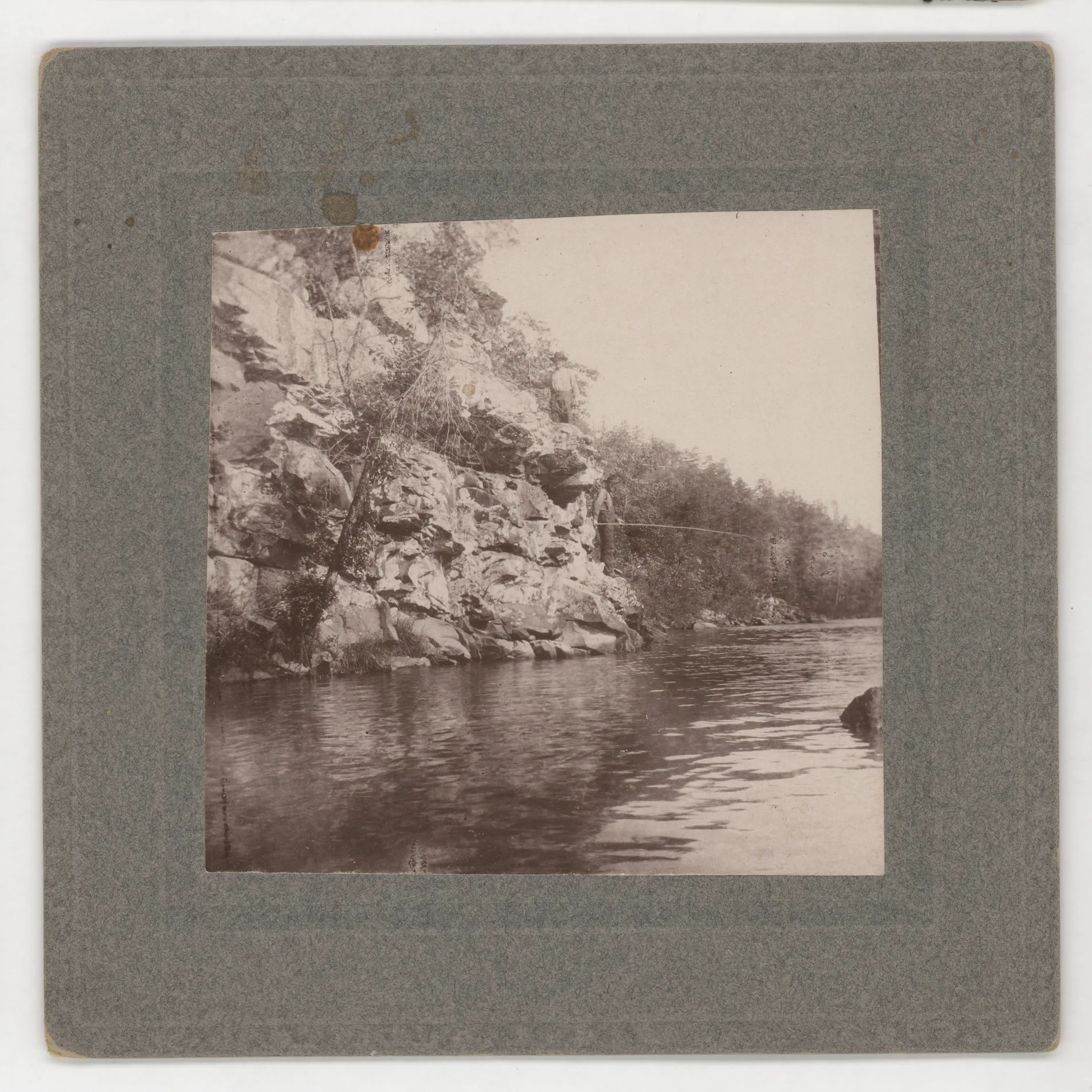 This photograph depicts John Swann fishing in an unknown lake or water source. There are two men depicted here.