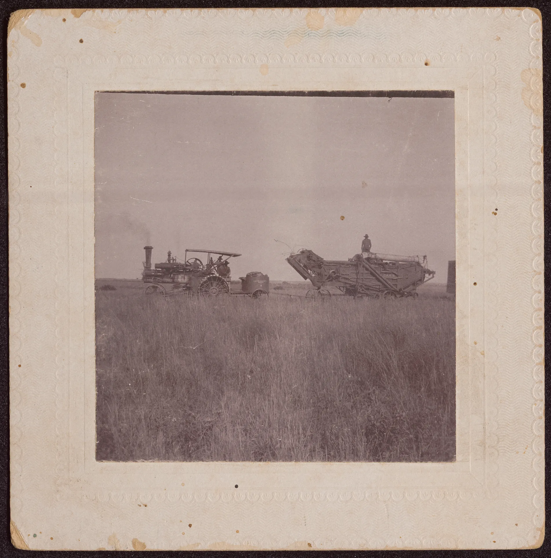 This photograph depicts a steam engine pulling a thresher in a wheat field. This photograph was likely taken in Oklahoma on one of the family's threshing excursions.